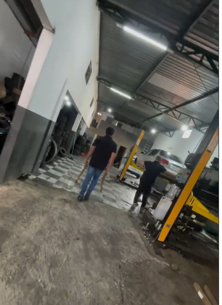 Interior da oficina da G2 Suspensão em Ceilândia, com carro no elevador e equipe trabalhando.